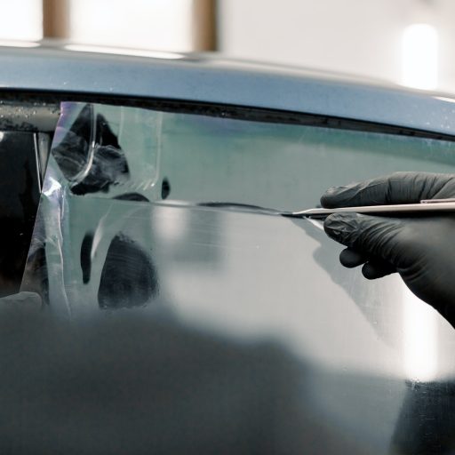 Cropped image of hands of worker in garage tinting a car window with tinted foil or film, holding